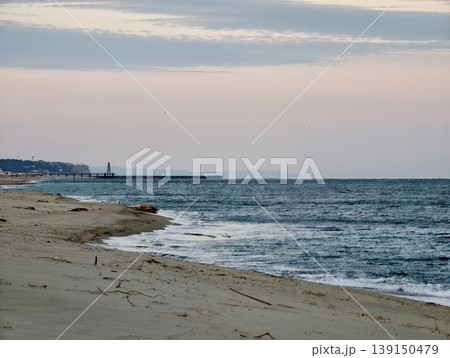 Serene shoreline with lighthouse silhouette. Calm coastal view featuring distant lighthouse and gentle waves Serene shoreline with lighthouse silhouette. Calm coastal view featuring distant lighthouse and gentle waves 139150479
