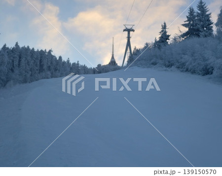Mountain slope with frosted trees. Calm winter scene featuring groomed trail and snowy pine forest Mountain slope with frosted trees. Calm winter scene featuring groomed trail and snowy pine forest 139150570