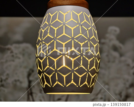 Handcrafted ceramic lamp casts golden glow. Contemporary ceramic pendant with intricate shadow patterns 139150817
