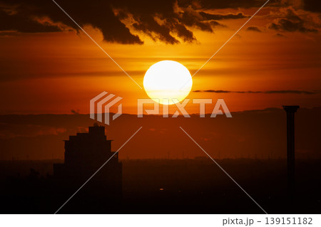 A large sun sets behind clouds in a dramatic red sunset sky 139151182