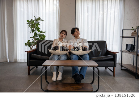 2人でソファに座って違う大きさの家のクラフトを持って考えている若いカップル 2人でソファに座って違う大きさの家のクラフトを持って考えている若いカップル 139151320