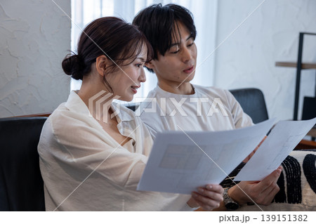 リビングのソファに座って家の図面を持って相談している若いカップル リビングのソファに座って家の図面を持って相談している若いカップル 139151382