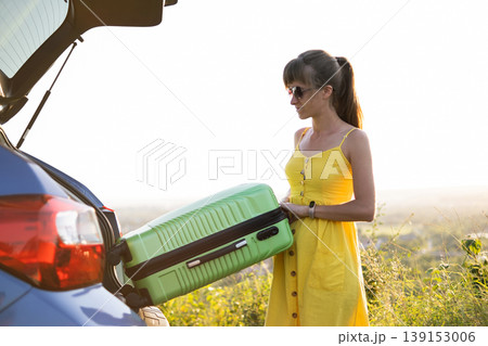 Young woman taking green suitcase from car trunk. Travel and vacations concept. Young woman taking green suitcase from car trunk. Travel and vacations concept. 139153006