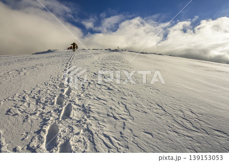 Wide view on the snowy hill with footprints and far away hiker walking up with backpack in the mountains Wide view on the snowy hill with footprints and far away hiker walking up with backpack in the mountains 139153053