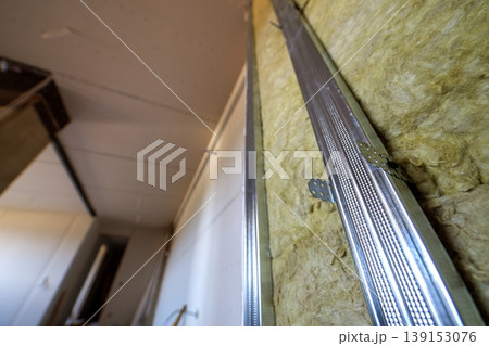 Wall of a room under renovation with mineral rock wool insulation and metal frame prepared for drywall plates. Wall of a room under renovation with mineral rock wool insulation and metal frame prepared for drywall plates. 139153076