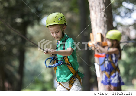 Two children, boy and girl in protective harness and safety helmets at climbing activity on rope way. 139153113