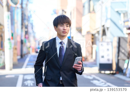 スマホを片手に街中を歩く外回り営業の若い日本人ビジネスマン スマホを片手に街中を歩く外回り営業の若い日本人ビジネスマン 139153570