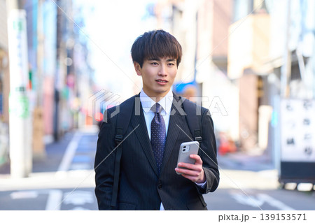 スマホを片手に街中を歩く外回り営業の若い日本人ビジネスマン スマホを片手に街中を歩く外回り営業の若い日本人ビジネスマン 139153571