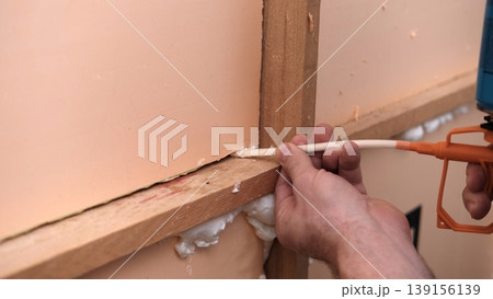 Applying thermal insulation foam with a gun. Using polyurethane foam along wall joints. Expanding the material. Sealing joints and soundproofing walls. Interior renovation. Close-up. Copy space. Applying thermal insulation foam with a gun. Using polyurethane foam along wall joints. Expanding the material. Sealing joints and soundproofing walls. Interior renovation. Close-up. Copy space. 139156139