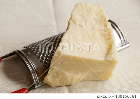 Close up of parmesan cheese wedge with metal grater on linen Close up of parmesan cheese wedge with metal grater on linen 139156561