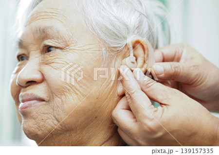 Doctor install hearing aid on senior patient ear to reduce hearing loss problem. 139157335