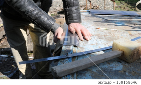 Strong male hands bend small sheets of metal on an outdoor workbench, with tools nearby, manual metalworking in a workshop, bending a piece of metal along the edge of a tabletop Strong male hands bend small sheets of metal on an outdoor workbench, with tools nearby, manual metalworking in a workshop, bending a piece of metal along the edge of a tabletop 139158646