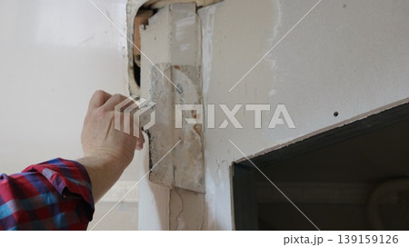 A spatula in the hand of a person repairing a wall under the ceiling above a doorway in a room near a rounded corner, patching a hole or gap when installing a room divider. A spatula in the hand of a person repairing a wall under the ceiling above a doorway in a room near a rounded corner, patching a hole or gap when installing a room divider. 139159126