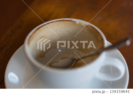 Close up of empty coffee cup with foam residue and spoon on wooden table warm cafe atmosphere finished drink moment and cozy morning break Close up of empty coffee cup with foam residue and spoon on wooden table warm cafe atmosphere finished drink moment and cozy morning break 139159645