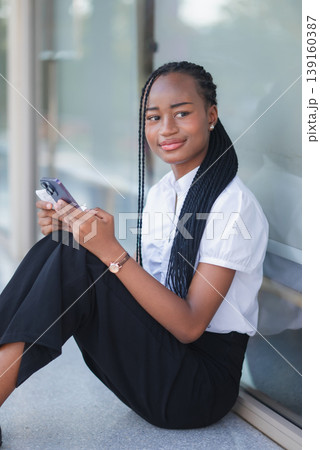 Young Black business woman seated outdoors with smartphone and paper receipt, looking thoughtful. Purchase verification, payment checking, budget review and digital banking concept. Young Black business woman seated outdoors with smartphone and paper receipt, looking thoughtful. Purchase verification, payment checking, budget review and digital banking concept. 139160387