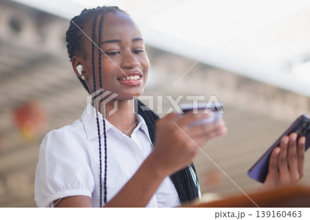 Smiling young Black woman making secure online payment with credit card and smartphone. Fintech transaction, mobile shopping, digital banking and cashless consumer lifestyle concept. 139160463