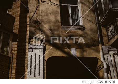 Dramatic urban contrast. Sunlight and deep shadows on the textured facade of an old European building with archway Fragment of historical house Dramatic urban contrast. Sunlight and deep shadows on the textured facade of an old European building with archway Fragment of historical house 139161516