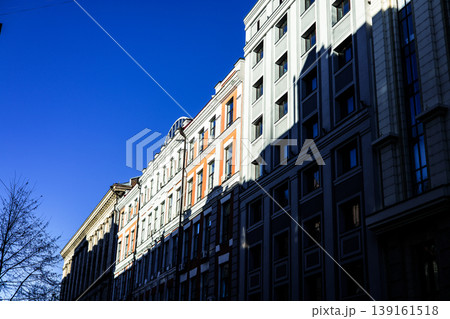 Dramatic urban contrast. Bright sunlight and deep shadow on modern and classic building facades with blue sky, symbolizing city life and modern architecture. A city street perspective view Real estate Dramatic urban contrast. Bright sunlight and deep shadow on modern and classic building facades with blue sky, symbolizing city life and modern architecture. A city street perspective view Real estate 139161518