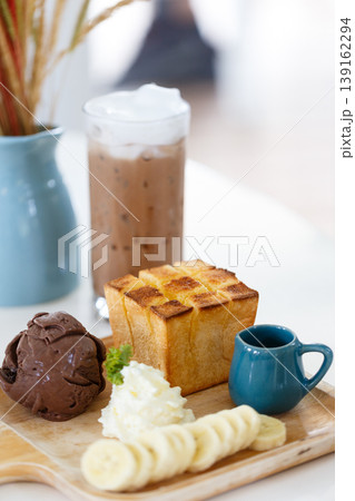 Warm French Toast Croissant Breakfast with Ice Cream Banana and Chocolate Drizzle Accompanied by Iced Coffee and Creamy Syrup 139162294
