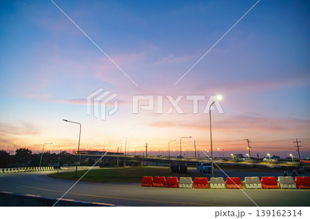Colorful sunset over a highway with streetlights and cars, captured during twilight with vibrant pastel sky and urban landscape backdrop Colorful sunset over a highway with streetlights and cars, captured during twilight with vibrant pastel sky and urban landscape backdrop 139162314