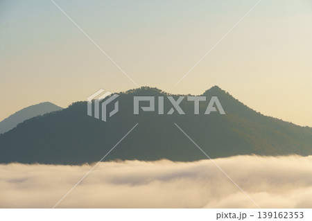 Serene mountain landscape with rolling hills covered in dense green forest and misty clouds at sunrise or sunset sky 139162353