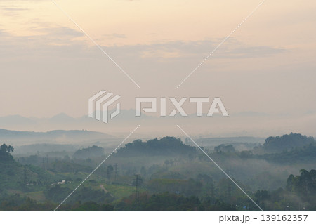 Misty mountain landscape with rolling hills and distant peaks under a soft, cloudy sky during early morning or late evening light 139162357