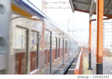 Blurred motion of a passenger train at a Japanese railway station platform. Abstract bokeh background of urban transit with bright orange pillars, morning sunlight, and high speed movement. Blurred motion of a passenger train at a Japanese railway station platform. Abstract bokeh background of urban transit with bright orange pillars, morning sunlight, and high speed movement. 139162432