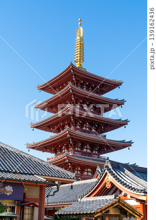 Majestic five-story red pagoda at Senso-ji Temple in Asakusa, Tokyo. This traditional Japanese Buddhist architecture features a golden spire under a clear blue sky with tiled roofs. 139162436