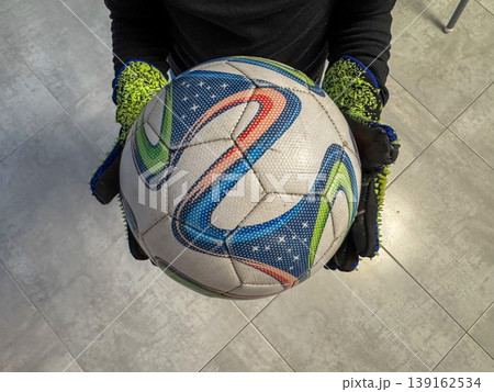 Player holds a colorful soccer ball with gloves in a training area during practice time Player holds a colorful soccer ball with gloves in a training area during practice time 139162534