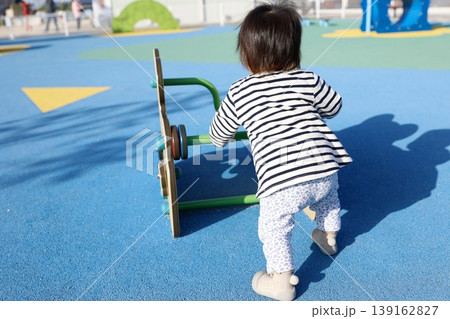 公園の遊具で遊ぶ1歳児の後ろ姿。青い舗装。 139162827
