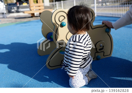 公園の遊具で遊ぶ1歳児の後ろ姿。青い舗装。 公園の遊具で遊ぶ1歳児の後ろ姿。青い舗装。 139162828