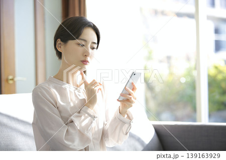 スマートフォンを確認する女性 自宅リビングでの落ち着いた時間 スマートフォンを確認する女性 自宅リビングでの落ち着いた時間 139163929