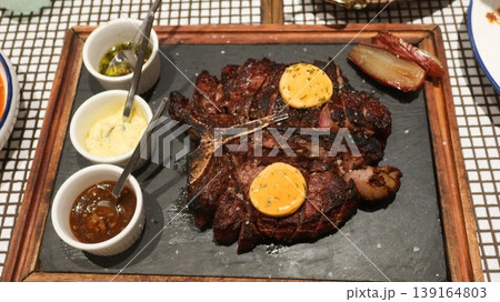 close up of a Grilled steak served on slate plate with melting herb butter, coarse salt, roasted shallot, and assorted sauces in ramekins of cream, pestle sauce and tomato sauce close up of a Grilled steak served on slate plate with melting herb butter, coarse salt, roasted shallot, and assorted sauces in ramekins of cream, pestle sauce and tomato sauce 139164803