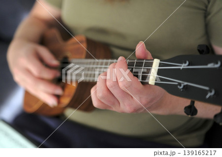 A man is playing a ukulele, close-up. The musician is looking for inspiration. Focus on the guitarist's hand healing the strings on the ukulele neck A man is playing a ukulele, close-up. The musician is looking for inspiration. Focus on the guitarist's hand healing the strings on the ukulele neck 139165217