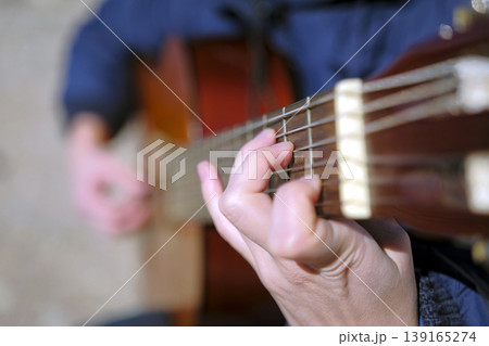 Close-up of a woman playing guitar, focus on finger and guitar strings. The image conveys a feeling of relaxation and enjoyment. The musician gives lessons Close-up of a woman playing guitar, focus on finger and guitar strings. The image conveys a feeling of relaxation and enjoyment. The musician gives lessons 139165274