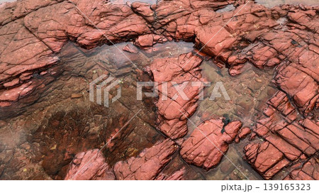 Layered deep reddish-brown sedimentary rock formations with fractures and water pools in the seaside which is a remote coastal spots in Hung Shek Mun (Red Stone Gate), Plover Cove Country Park, Hong Layered deep reddish-brown sedimentary rock formations with fractures and water pools in the seaside which is a remote coastal spots in Hung Shek Mun (Red Stone Gate), Plover Cove Country Park, Hong 139165323