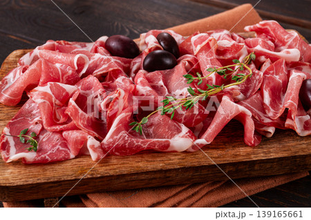 Freshly cut dried meat, served with olives and herbs, on a wooden chopping board, no people, Freshly cut dried meat, served with olives and herbs, on a wooden chopping board, no people, 139165661