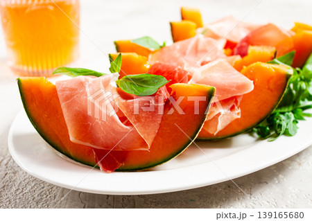 Cantaloupe melon with prosciutto and fresh basil, on a white plate, natural light, Cantaloupe melon with prosciutto and fresh basil, on a white plate, natural light, 139165680