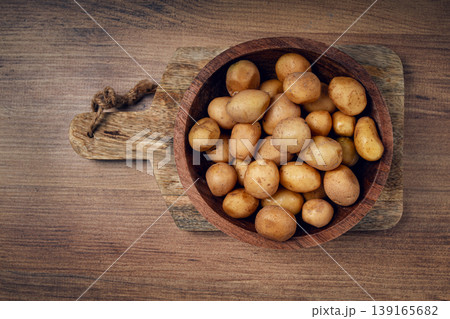 Freshly harvested small potatoes in a wooden bowl on a rustic cutting board 139165682