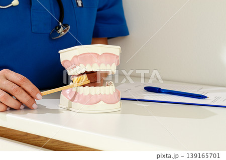 A dentist in a blue uniform demonstrates the correct technique of brushing teeth, on a model, in a clinical setting, A dentist in a blue uniform demonstrates the correct technique of brushing teeth, on a model, in a clinical setting, 139165701