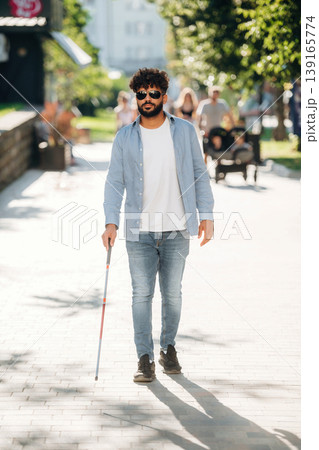Under beautiful sunlight, walking. Blind man with white cane and sunglasses is in the city Under beautiful sunlight, walking. Blind man with white cane and sunglasses is in the city 139165774