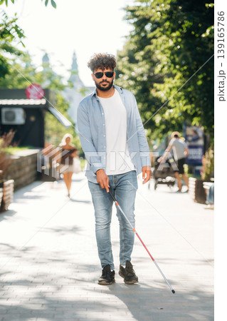 Wearing casual clothes, having a walk. Blind man with white cane and sunglasses is in the city 139165786