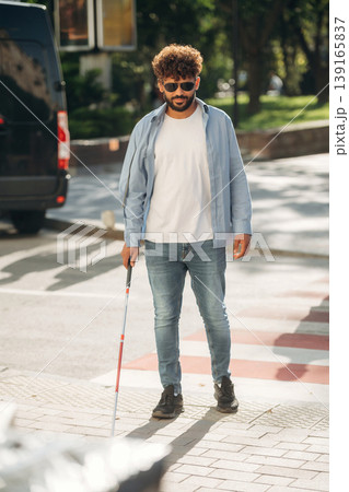 Wearing casual clothes, having a walk. Blind man with white cane and sunglasses is in the city Wearing casual clothes, having a walk. Blind man with white cane and sunglasses is in the city 139165837