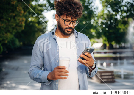 Paper cup in right hand and smartphone in left one. Handsome man is outdoors in the city Paper cup in right hand and smartphone in left one. Handsome man is outdoors in the city 139165849