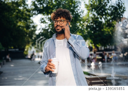 Paper cup in right hand and smartphone in left one. Handsome man is outdoors in the city 139165851