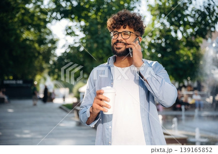 Paper cup in right hand and smartphone in left one. Handsome man is outdoors in the city 139165852