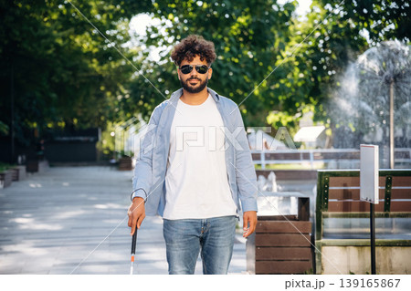 Having a walk, using cane stick. Blind man with white cane and sunglasses is in the city 139165867