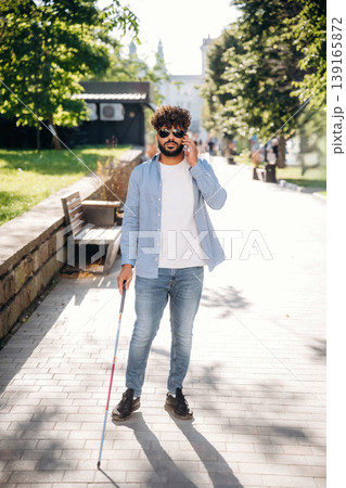 Talking by phone. Blind man with white cane and sunglasses is in the city 139165872