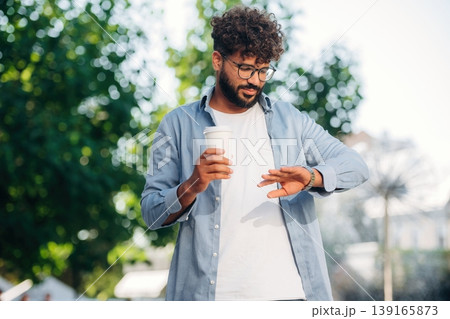 Checks the time, looks at his wristwatch. Handsome man is outdoors in the city Checks the time, looks at his wristwatch. Handsome man is outdoors in the city 139165873