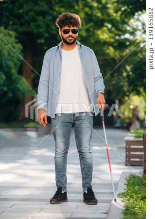 Using cane stick. Blind man in sunglasses is in the city 139165882